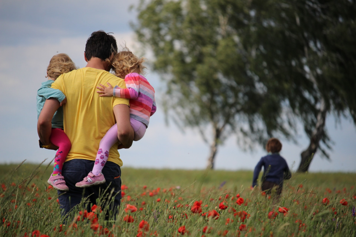 Egy apuka három kisgyermekével sétál a mezőn.